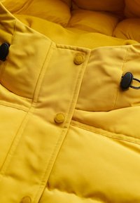 Gul polstret jakke med en glat stofoverflade, trykknapper og snoretræk ved kraven.