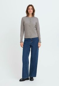Cardigan en tricot gris avec un col rond et une fermeture à boutons sur le devant. Présente des poignets et un ourlet côtelés, porté sur un jean ample bleu.