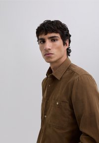 Bruine overhemd met knopen, gemaakt van een gestructureerde stof, met een spitse kraag, een borstzak en zichtbare knopen aan de voorkant.