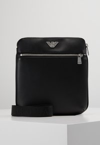 Borsa a tracolla in pelle nera con logo argentato, chiusura con zip e superficie testurizzata. Include una tracolla regolabile abbinata.