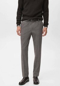 Pantaloni grigi a motivo houndstooth con vestibilità tailored, realizzati in tessuto testurizzato. Indossati con un maglione scuro a coste e stivaletti neri.