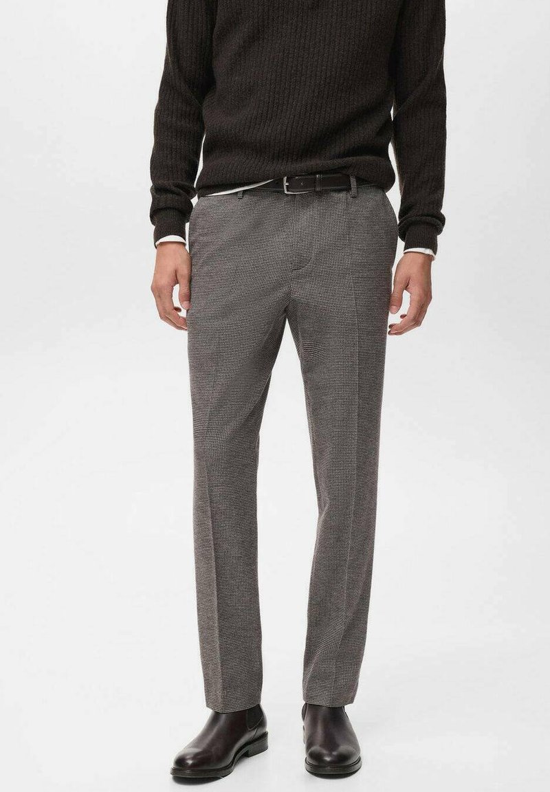 Pantaloni grigi a motivo houndstooth con vestibilità tailored, realizzati in tessuto testurizzato. Indossati con un maglione scuro a coste e stivaletti neri.