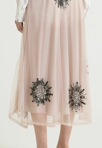 Jupe en tulle rose avec deux appliqués floraux en noir et argent ornés; texture douce avec un design fluide, coupe mi-genou.