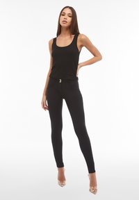 Top a canottiera nera a costine abbinato a leggings neri a vita alta con chiusura a doppio bottone e tasche, completato da tacchi trasparenti.