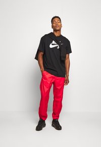 Black Nike t-shirt with logo, red shiny sweatpants, and black sneakers. The outfit features a sweatshirt draped over the shoulders.