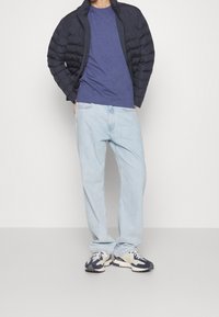Námořnická puffer bunda, modré tričko, světlé uvolněné džíny a tenisky s námořnickými a smetanovými akcenty. Neformální, vrstvený outfit.