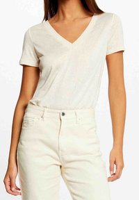 T-shirt crema con scollo a V realizzata in materiale leggero e morbido, con maniche corte e una vestibilità comoda, abbinata a pantaloni chiari.