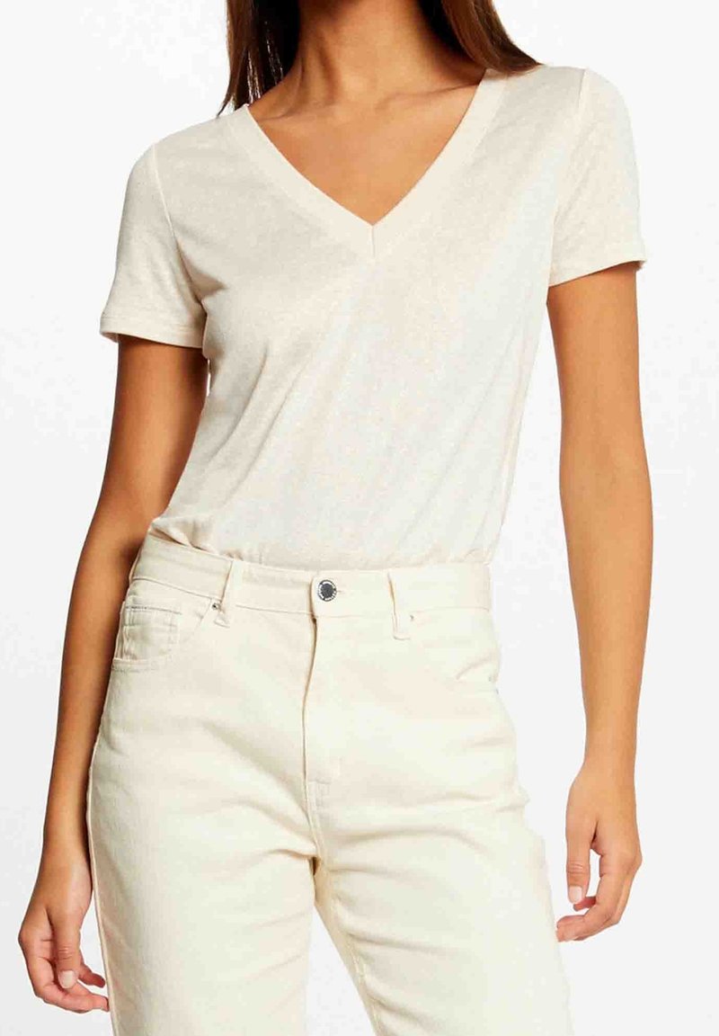 T-shirt crema con scollo a V realizzata in materiale leggero e morbido, con maniche corte e una vestibilità comoda, abbinata a pantaloni chiari.