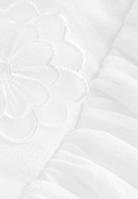 Biely textil s kvetinovým vyšitým vzorom s vystúpeným stehom. Vedľa sa nachádza riasená textúra s hladkým povrchom.