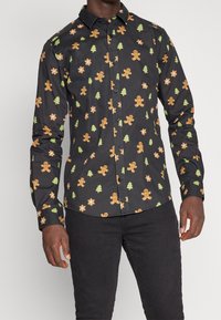 Camicia nera con bottoni, decorata con un motivo di omini di pan di zenzero, alberi verdi e stelle arancioni e verdi. Maniche lunghe, vestibilità sartoriale.