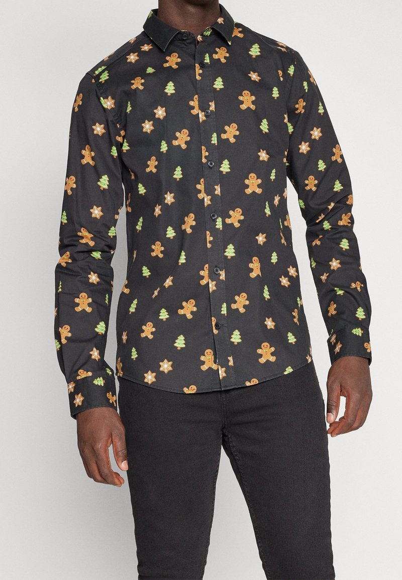 Camicia nera con bottoni, decorata con un motivo di omini di pan di zenzero, alberi verdi e stelle arancioni e verdi. Maniche lunghe, vestibilità sartoriale.