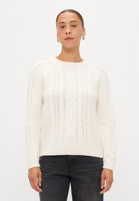 Maglione bianco a maglia grossa con polsini e orlo a coste, che presenta motivi testurizzati in rilievo e un classico scollo tondo.