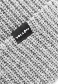 Grau gestrickte Mütze mit einem strukturierten Muster. Ein schwarzes Etikett mit weißem Text "VOLCOM" ist an der Seite sichtbar.