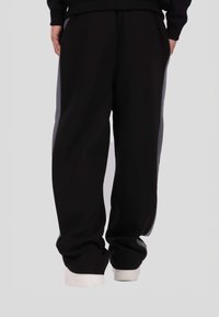Czarne spodnie dresowe z szarymi bocznymi panelami, luźnym krojem i elastycznym pasem. Posiadają przednie kieszenie i miękką fakturę. Widoczne białe buty.