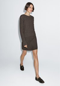 Braunes Strickpullover- und passenden Rock-Set mit Rundhalsausschnitt, langen Ärmeln sowie gerippten Bündchen und Saum; kombiniert mit dunklen Slippern.