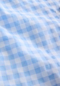 Tissu à carreaux bleu clair et blanc avec un tissage texturé et des plis subtils et des ombres visibles.