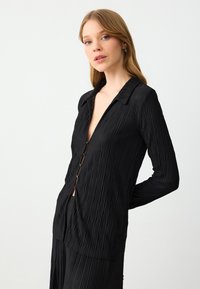Zwarte plissé blouse met knopen, een kraaglijn en lange mouwen, met een gestructureerde stof en een diepe V-hals.