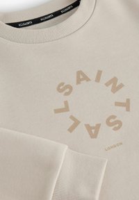 Bežna dukserica z ribastim izrezom in manšetami. Ima krožno grafiko v svetlo rjavi barvi z napisom "SAINT" in "LONDON". Mehka tekstura.