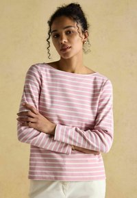 Svetlo ružová košeľa s dlhým rukávom, biele horizontálne pruhy, okrúhly výstrih a mäkká bavlnená textúra, nosená s prekríženými rukami.