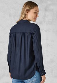 Camicia a maniche lunghe blu navy con schiena plissettata, polsini con bottoni e orlo curvo, realizzata in un tessuto liscio.