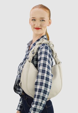 Beige leren handtas met een unieke, stevige handgreep, die op de schouder wordt gedragen. De tas heeft een afgeronde vorm en een ritssluiting.