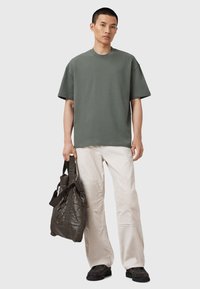 Grøn bomulds T-shirt med korte ærmer, parret med cremefarvede vide bukser og en mørk quiltet taske med skulderremme.