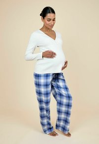 Tehotenský outfit pozostávajúci z krémového trička s dlhým rukávom a výstrihom do V a svetlomodrých kockovaných pyžamových nohaviciach s elastickým pásom a šnúrkou.