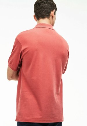 Polo a maniche corte in corallo, realizzato in cotone liscio. Presenta un colletto classico e un orlo dritto. La vista posteriore mostra dettagli minimi.