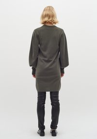 Mörkgrön långärmad stickad klänning med puffiga axlar, i kombination med svarta läderbyxor och skor. Minimalistisk design, enkel textur.