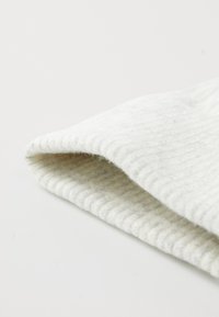 Tissu en laine tricoté côtelé gris clair, plié pour montrer la texture et l'épaisseur, avec une surface douce et duveteuse près des bords.