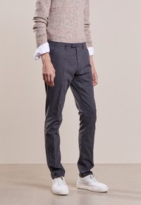 Pantaloni grigi su misura con una texture liscia e pieghe stirate, abbinati a un maglione beige in maglia e scarpe da ginnastica bianche.