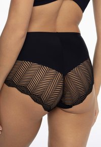 Czarne majtki z wysokim stanem, ozdobione koronką w wzór zygzaka. Tkanina jest gładka na górze i teksturowana poniżej.