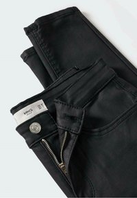 Zwarte denim jeans met een gladde textuur, voorzien van een metalen rits, zilveren knoop en een witte stoffen label aan de binnenkant van de tailleband.