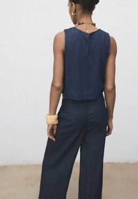 Donkerblauwe denim crop top met een eenvoudige achternaad. Gestyled met een wijde marineblauwe broek, met een soepele textuur en minimale details.
