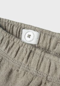 Hellgrauer, strukturierter Stoff mit einem elastischen Bund, der einen weißen Knopf und gestickte Details aufweist, mit einem Nahaufnahme des oberen Rands.