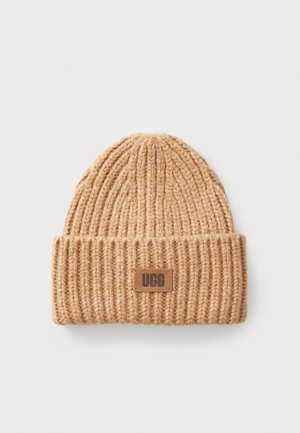 Kootud beanie heledas pruunis, ribade tekstuuriga ja voltimisega äärega. Omab väikest, ristkülikukujulist UGG logo silti beežis värvuses.