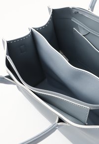 Borsa a mano in pelle grigia con più scomparti, cuciture bianche, texture liscia e tasca con zip. L'interno presenta un design semplice.