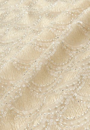 Béžová látka s prepracovanými vlnitými vzormi, zdobená striebornými flitrami a korálkami, vytvárajúca štruktúrovaný a dekoratívny povrch.