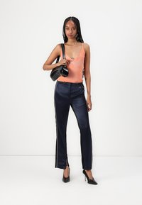 Orange sleeveless top, navy satin pants with white side stripes, paired with black high heels and a shiny black handbag.
