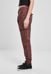 Bordó cargo kalhoty s tapered designem, elastickými manžetami, bočními kapsami a zapínáním na knoflík. Nosené s černými teniskami.