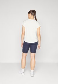 Vit kortärmad skjorta med lätt struktur, matchad med marinblå cykelbyxor. Modellen bär vita sneakers och ankelsockor; står framför en enfärgad bakgrund.