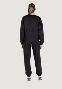 Set di felpa nera e pantaloni sportivi realizzati in tessuto morbido, caratterizzati da una vestibilità rilassata e polsini a costine, abbinati a sneakers con motivo.