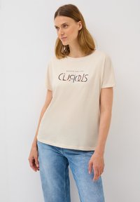 Ljusbeige bomulls t-shirt med korta ärmar och rundad halsringning, med ett tryckt motiv i mörka och ljusa färger.