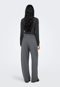 Calças cinzentas de perna larga com cintura elástica e dois bolsos traseiros, combinadas com uma camisola de malha macia de manga comprida em tom cinza escuro.