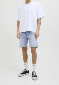 Vit oversized t-shirt, ljusblå denimshorts, svarta sneakers med vita sulor och vita strumpor med logotyp. Avslappnad sommaroutfit.