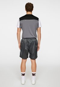 Träningsoutfit bestående av en grå och svart kortärmad tröja samt blanka svarta shorts. Inkluderar vita detaljer och elastisk midja.