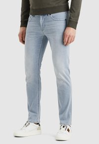 Svijetloplave traperice slim fit kroja, s pet džepova i suptilnom izblijedjelom teksturom, uparené s bijelim tenisicama.