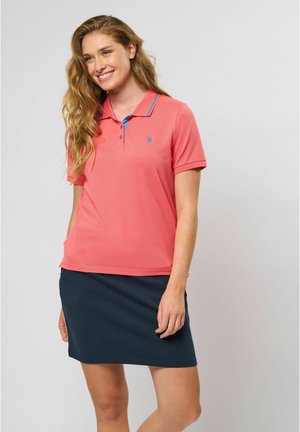 Rožinė polo marškinė su mėlynomis detalėmis, trumpomis rankovėmis ir mažu logotipu. Derinama su tamsiai mėlynomis sijonais, suteikiančiais atsipalaidavusį, sportišką įvaizdį.