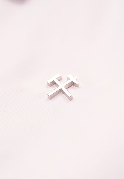 Κονκάρδα με σύμβολο εξόρυξης αργύρου με διασταυρωμένο σφυρί και πικά στο ανοιχτό ροζ φόντο υφάσματος.