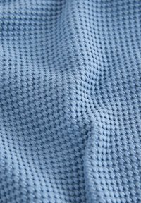Helle blaue Stoff mit einer strukturierten Waffelwebung, die weiche, feine Fasern zeigt, die Tiefe und subtile Farbnuancen erzeugen.